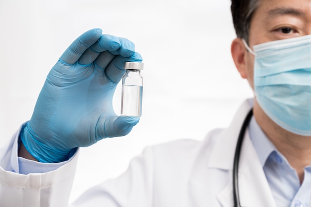 La main du médecin portant des gants bleus sur fond blanc et tenant le vaccin Covid-19.