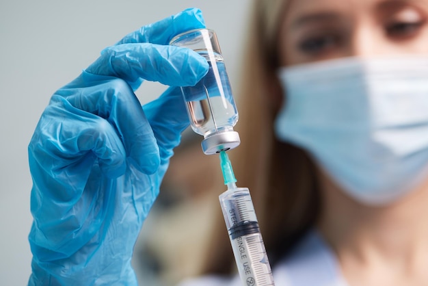 La main du médecin porte un gant médical tenant une seringue tout en prenant un vaccin liquide d'un flacon sur le point d'être injecté Concept de vaccination par injection