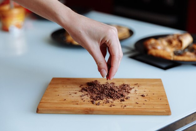 La main du pâtissier avec du chocolat râpé Va saupoudrer le gâteau