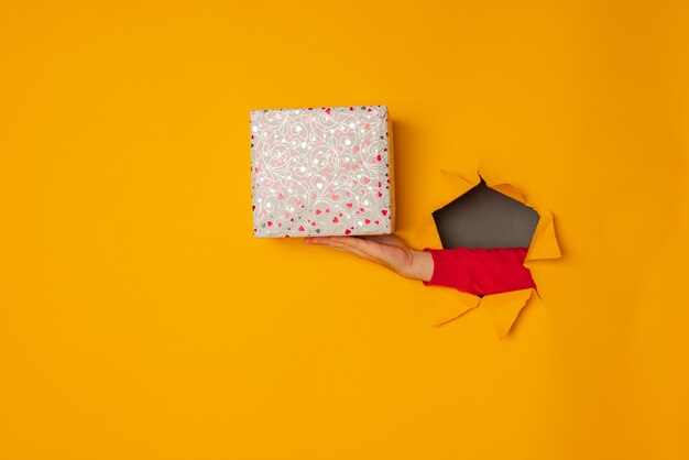 La main du père Noël tenant une boîte avec un cadeau dans le fond jaune du trou