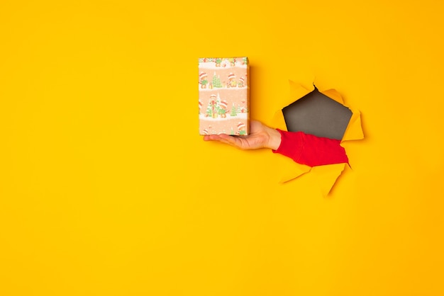 La main du père Noël tenant une boîte avec un cadeau dans le fond jaune du trou