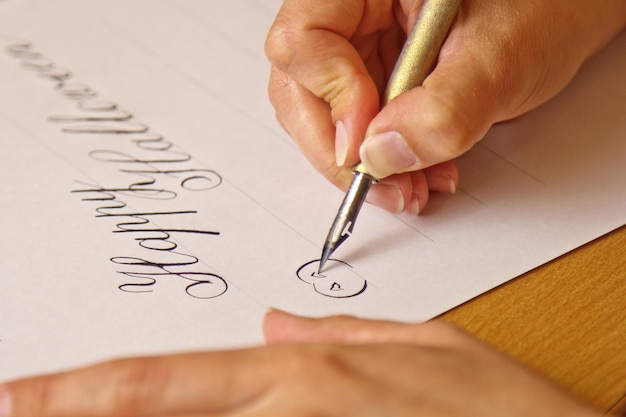 La main écrit avec le stylo à encre le joyeux halloween sur une feuille de papier blanc avec des rayures papeterie sur le bureau gros plan vue de dessus leçons d'orthographe et exercices de caligraphie Arrière-plan de mise en page du modèle