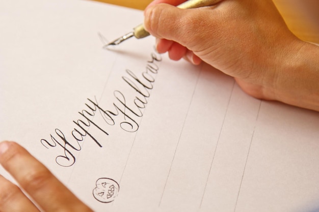 Photo la main écrit avec le stylo à encre le joyeux halloween sur une feuille de papier blanc avec des rayures papeterie sur le bureau gros plan vue de dessus leçons d'orthographe et exercices de caligraphie arrière-plan de mise en page du modèle