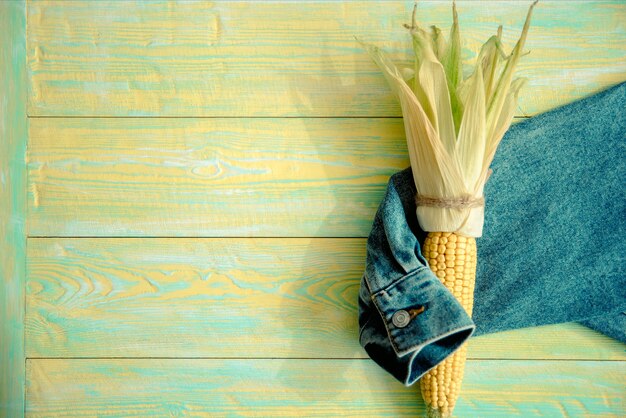 La main embrasse un bouquet d'épis de maïs, veste en jean, vue de dessus.