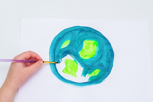 Main d'enfant dessinant une planète Terre avec une carte du monde à l'aquarelle sur papier blanc. Concept du jour de la paix et de la terre. Vue de dessus.