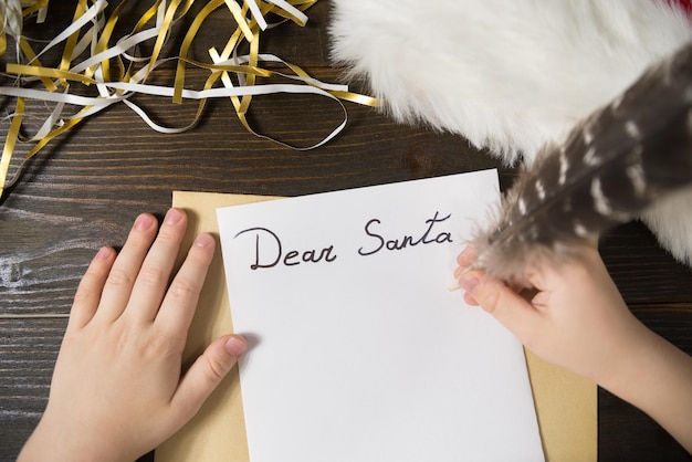 La main d'enfant écrit la lettre au fond en bois de Santa Tinsel