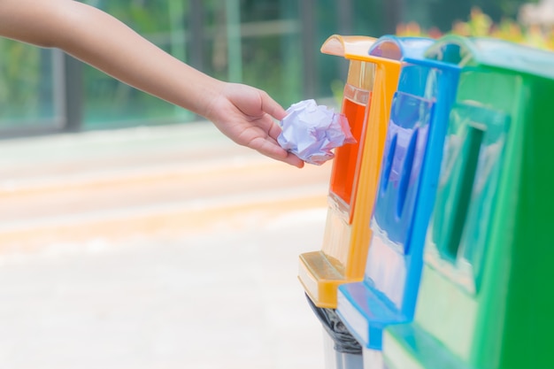 Une main d&#39;enfant jetant du papier froissé dans un bac de recyclage. Concept de la journée mondiale de l&#39;environnement.