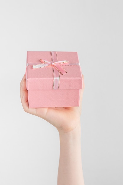 Photo main d'enfant tenant une boîte-cadeau avec noeud rose fond blanc et gris avec espace de copie