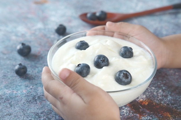 Main de l'enfant tenant un bol de yogourt frais avec des baies bleues