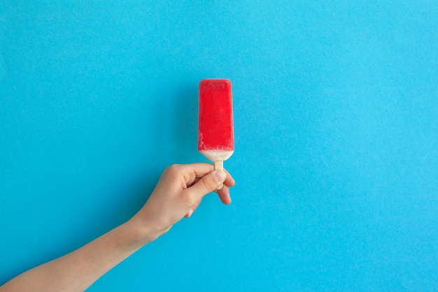 Main d'enfant tenant une glace à la fraise rouge sur fond bleu
