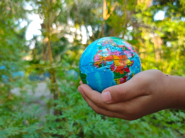 La main d'un enfant tient un globe terrestre avec un fond de nature verdoyante Le concept de l'avenir de la terre et des enfants