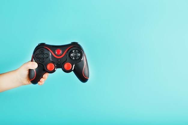 La main de l'enfant tient triomphalement la manette de jeu sur une surface bleue