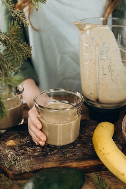 La main de l'enfant avec un verre de smoothie fraîchement préparé près du mélangeur et des fruits