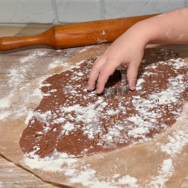 La main des enfants coupe des biscuits de Noël avec des emporte-pièces forme une table en bois de farine