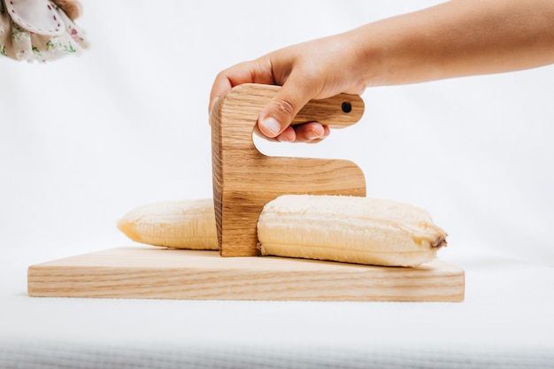 La main des enfants avec un couteau en bois et une banane sur une planche à découper