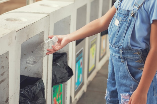Photo main d'enfants jetant une bouteille en plastique vide dans la poubelle recyclage au parc