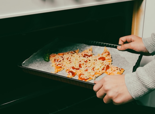 La main des enfants pose un plat allant au four avec une pizza sapin de noël au four