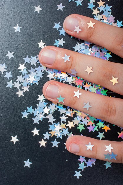 Photo main sur des étoiles de confettis colorées sur un fond de couleur sombre