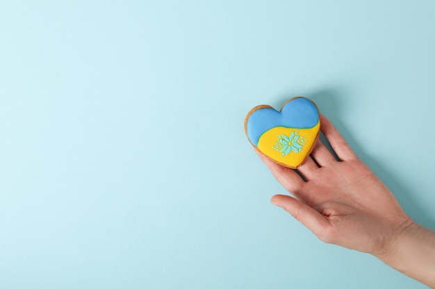 La main femelle tient le biscuit avec des couleurs de drapeau de l'Ukraine sur le fond bleu