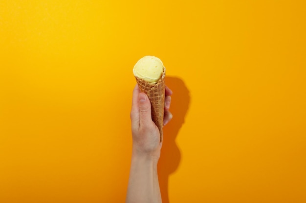 La main femelle tient la crème glacée sur le fond orange