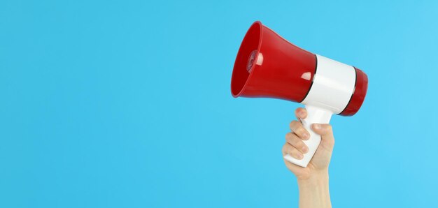 La main femelle tient le mégaphone sur le fond bleu