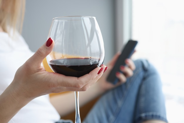 La main femelle tient le verre de vin et le smartphone