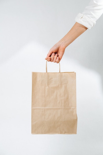 Main féminine apportant un sac en papier brun vide sur fond blanc.