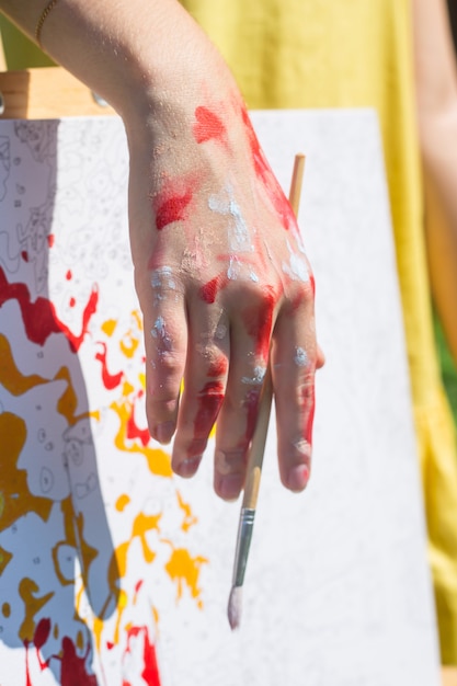 La main féminine de l&#39;artiste maculée de peinture tient un pinceau