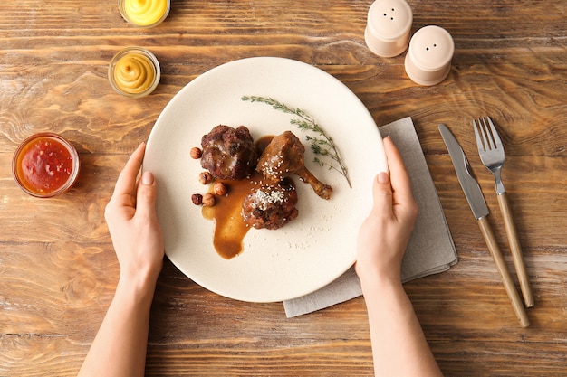Main féminine et assiette avec de savoureuses sucettes au poulet sur une surface en bois