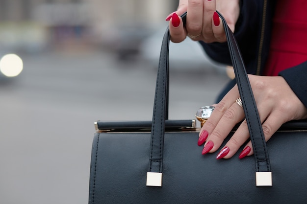 Main féminine avec une belle manucure rouge ouvrant un sac à main en cuir noir. Espace libre