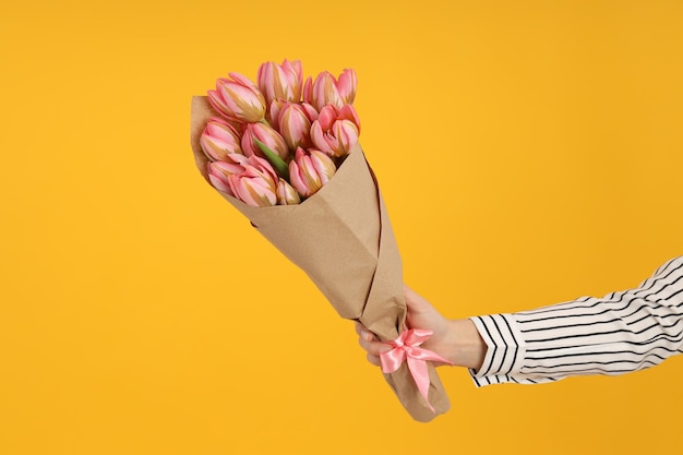 Main féminine avec bouquet de tulipes sur fond jaune