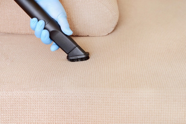 Une main féminine dans un gant aspire la surface du canapé