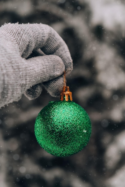 Photo main féminine dans les gants boule de noël à la mode brillante verte sur les sapins de branche enneigée en hiver forestholiday