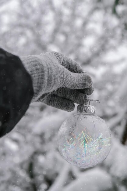 Photo main féminine dans les gants boule de noël en verre tendance transparente sur les sapins enneigés dans la forêt d'hiver