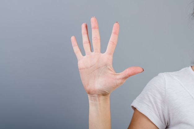 Main féminine dans le poing montrant cinq doigts isolés sur gris