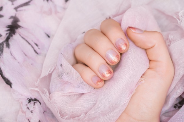 Main féminine avec un design ongle scintillant rose.