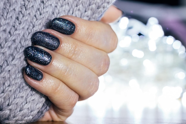 Main féminine avec écharpe tricotée grise et manucure festive ongles scintillants bleus au nouvel an ou à la fête de Noël Mise au point sélective Vue rapprochée avec espace de copie