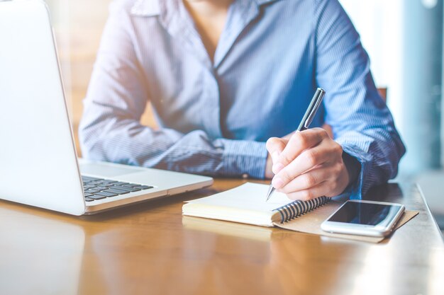 Main féminine écrit sur le bloc-notes avec un stylo au bureau