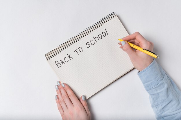 Une main féminine écrit dans le bloc-notes un mot RETOUR À L'ÉCOLE. Vue de dessus