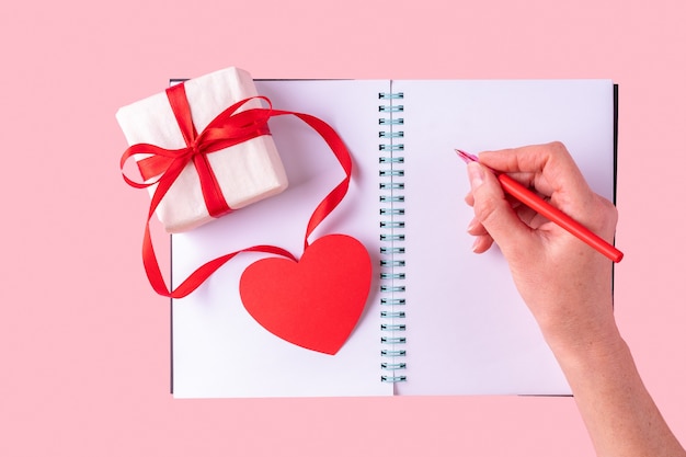 La main féminine écrit un message d'amour avec un stylo rouge dans un cahier ouvert blanc blanc