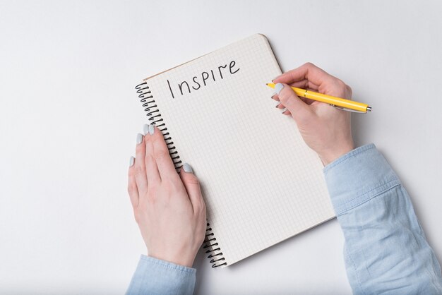 Main féminine écrit le mot inspirer dans le cahier. Bloc-notes et stylo, fond blanc