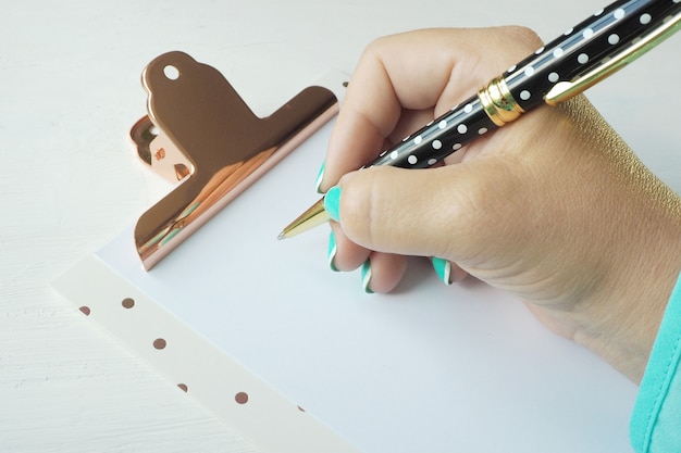 Une main féminine écrit avec un stylo à bille sur une feuille de papier vierge dans un presse-papiers.