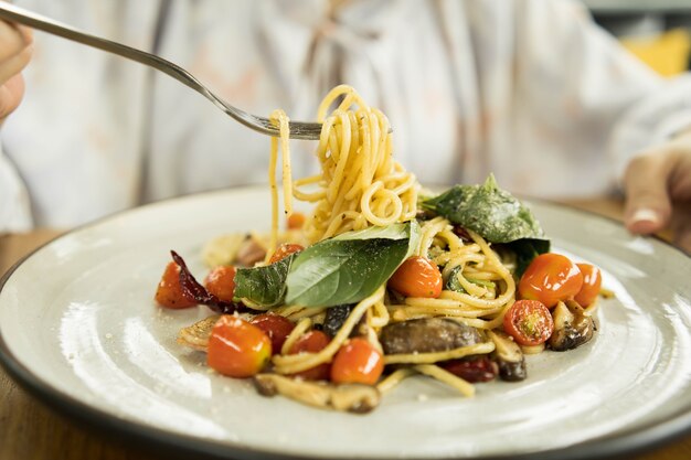 Une main féminine essaie d'utiliser une fourchette pour manger des spaghettis épicés avec du bacon et du basilic garnis de fromage râpé dans le plat blanc.