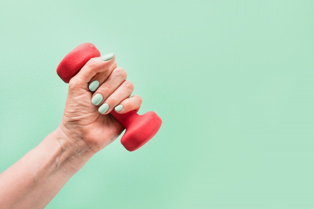 Main féminine avec haltère rouge sur fond vert