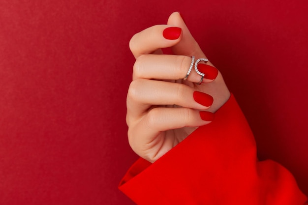 Main féminine avec manucure tendance sur fond rouge, design d'ongles rouge mat