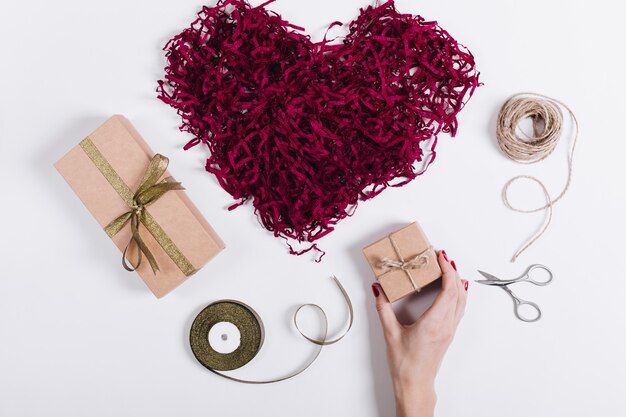 Une main féminine met des boîtes avec des cadeaux près d&#39;un cœur décoratif rouge