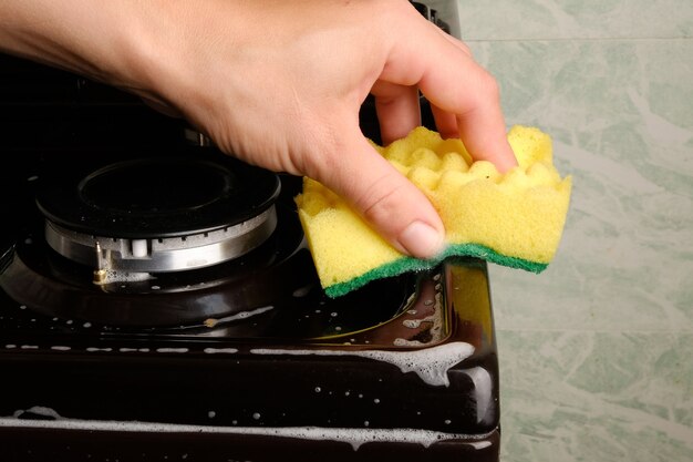 Une main féminine nettoie la cuisinière à gaz avec une éponge avec de la mousse blanche, nettoyant la surface. hygiène à la maison, électroménagers.