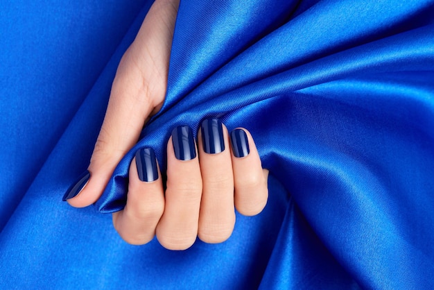 Main féminine avec des ongles bleus tenant un tissu de satin bleu