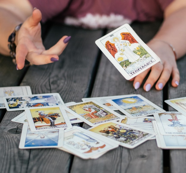 Une main féminine avec des ongles violets lance une carte de tarot nommée Tempérance sur la surface de la planche avec des cartes de tarot disposées face visible. Minsk, Biélorussie, 28.07.2021