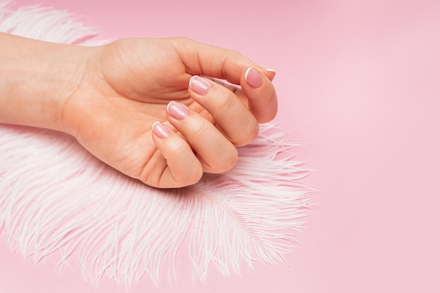 Main féminine avec une peau lisse et une plume d'autruche douce sur fond rose